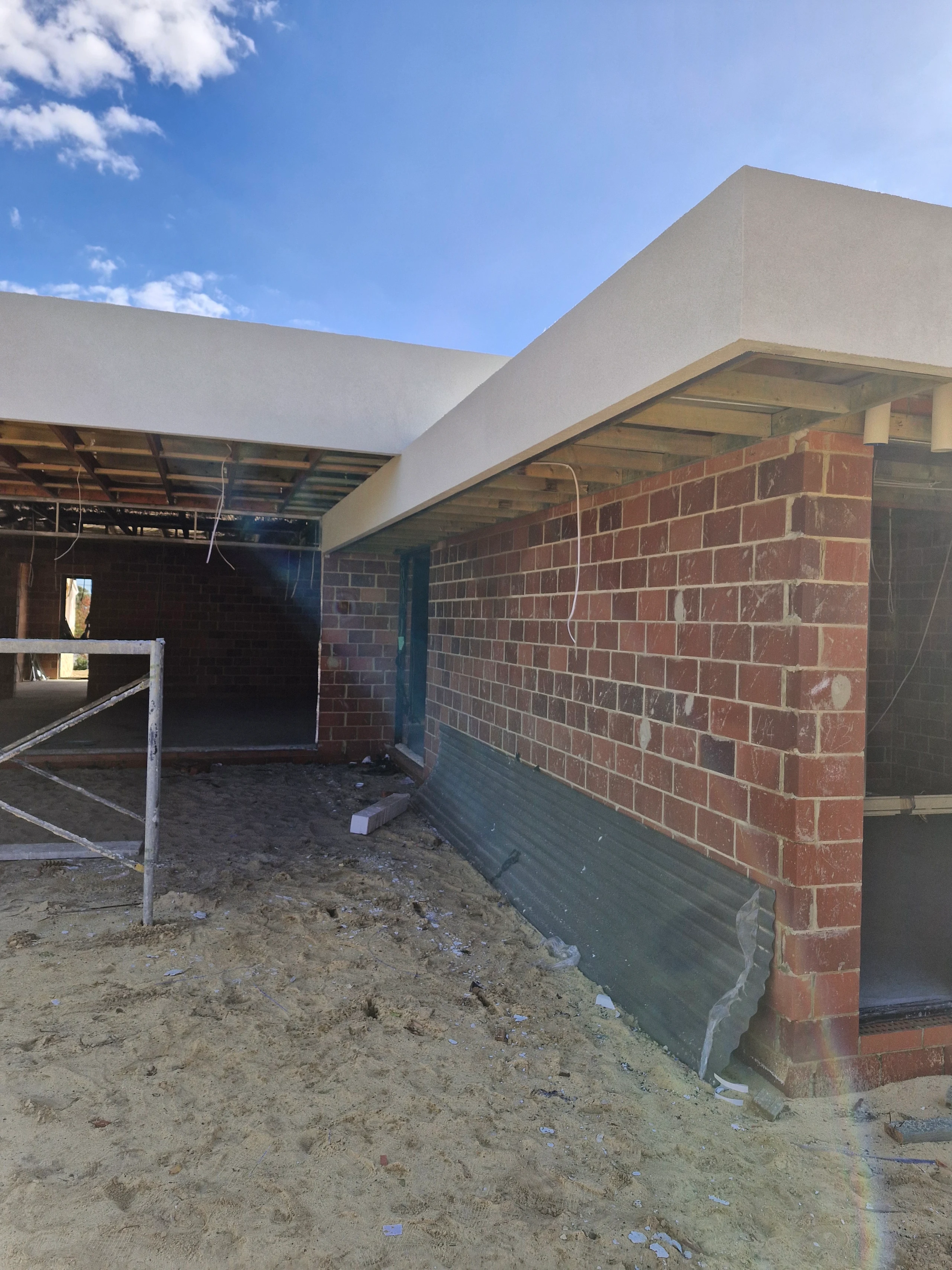 Finished white parapets above exposed brick walls and framing around an unfinished entry.