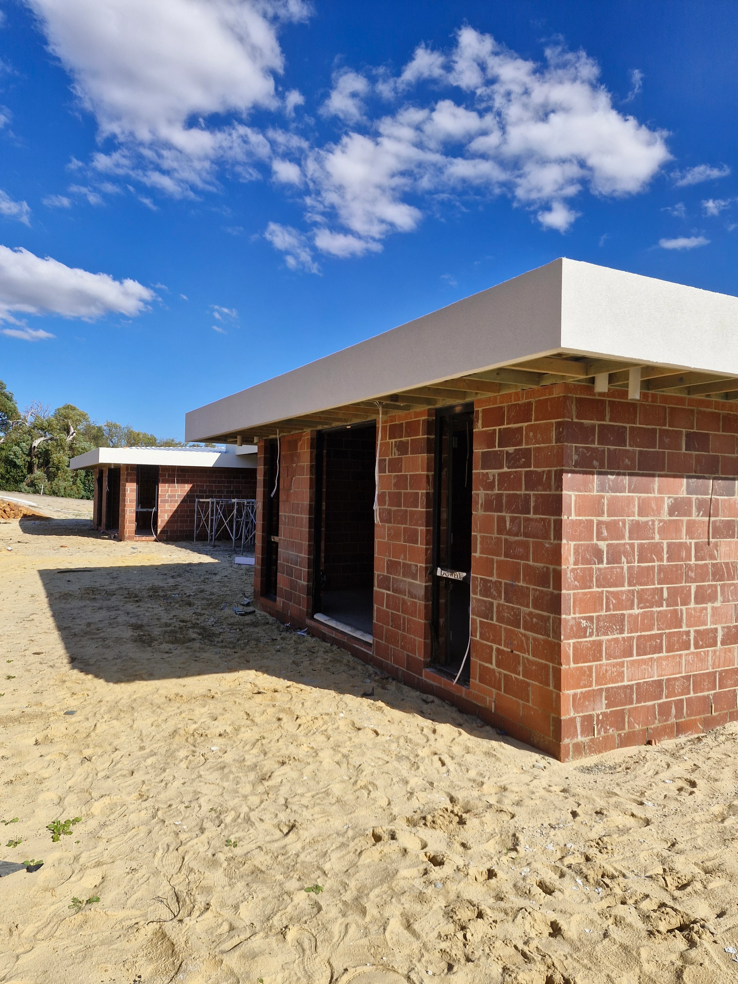White finished roofline above an unfinished brick entry and exposed framing.