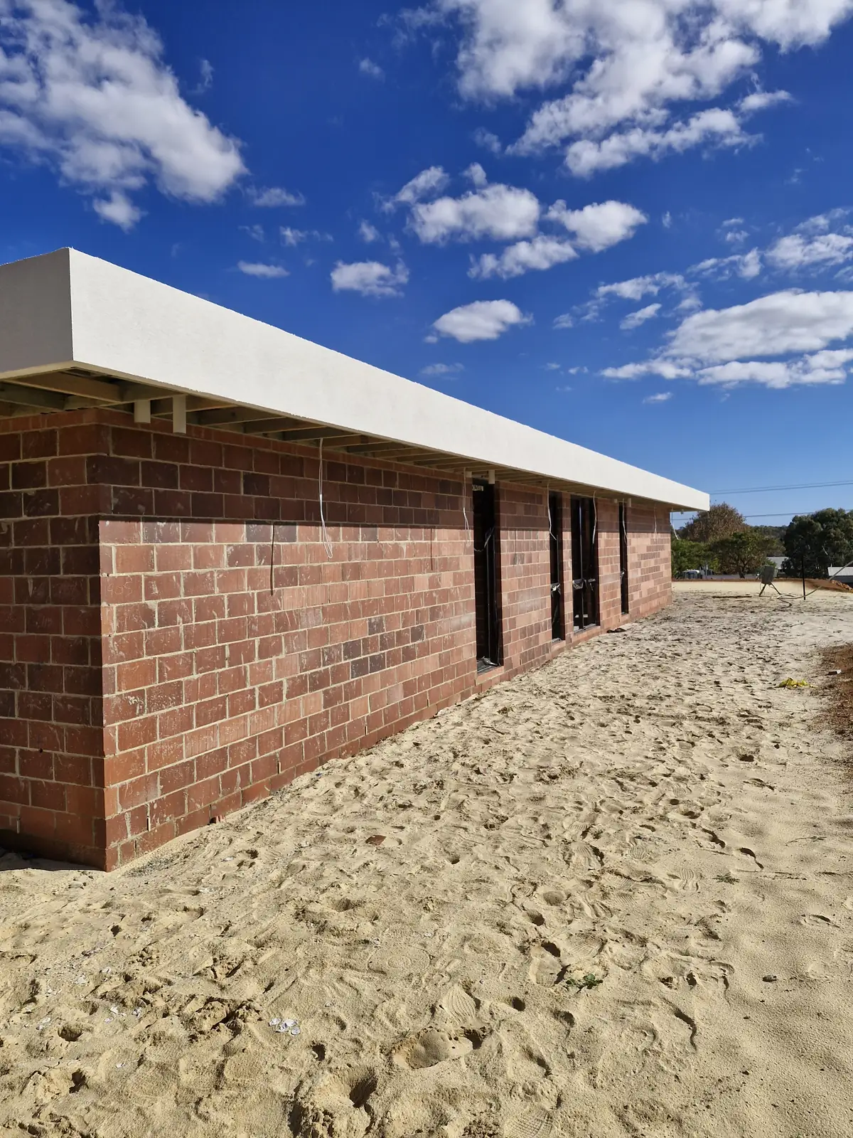 Long white finished parapet above exposed brick walls on a building site.