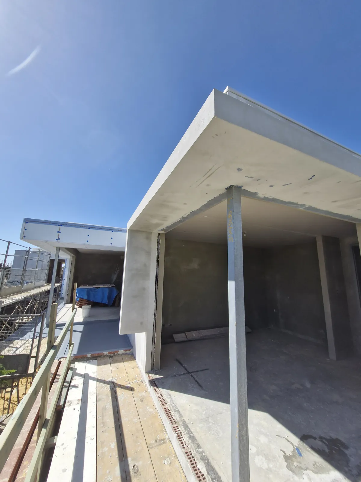 Pale projecting facade panels around an unfinished opening beside a scaffold walkway.