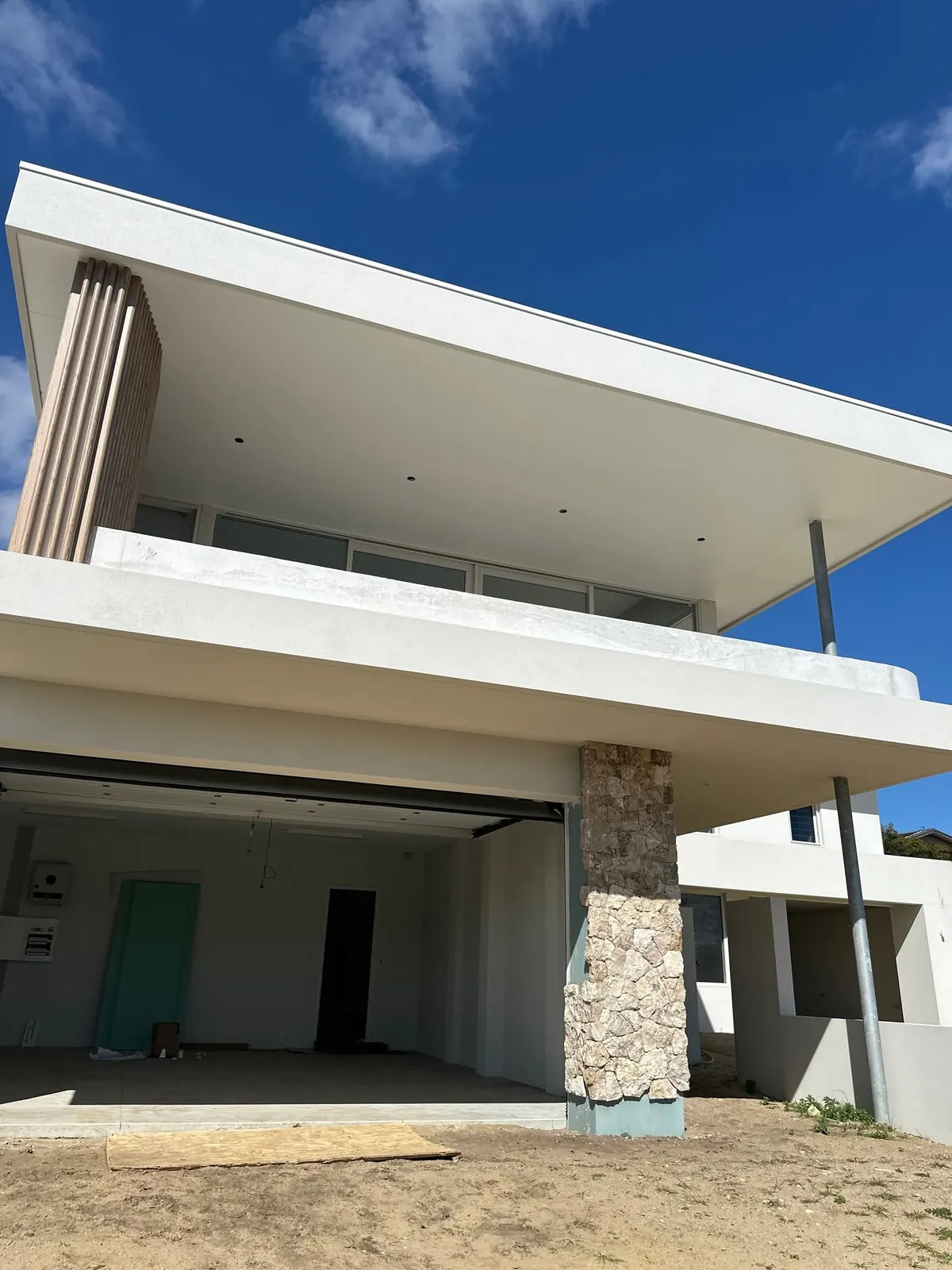 White balcony facade with stone-clad columns and an unfinished garage opening.