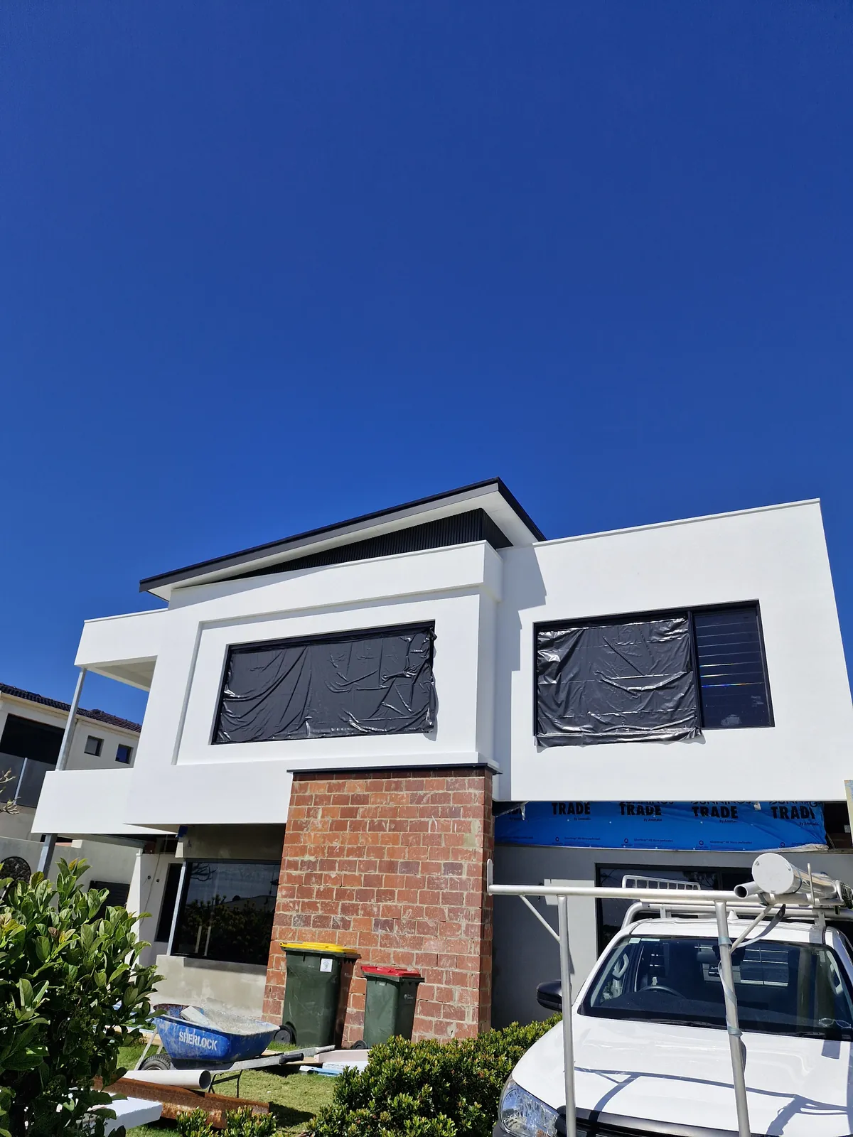 White upper facade with covered windows above exposed brickwork and blue wrap during construction.