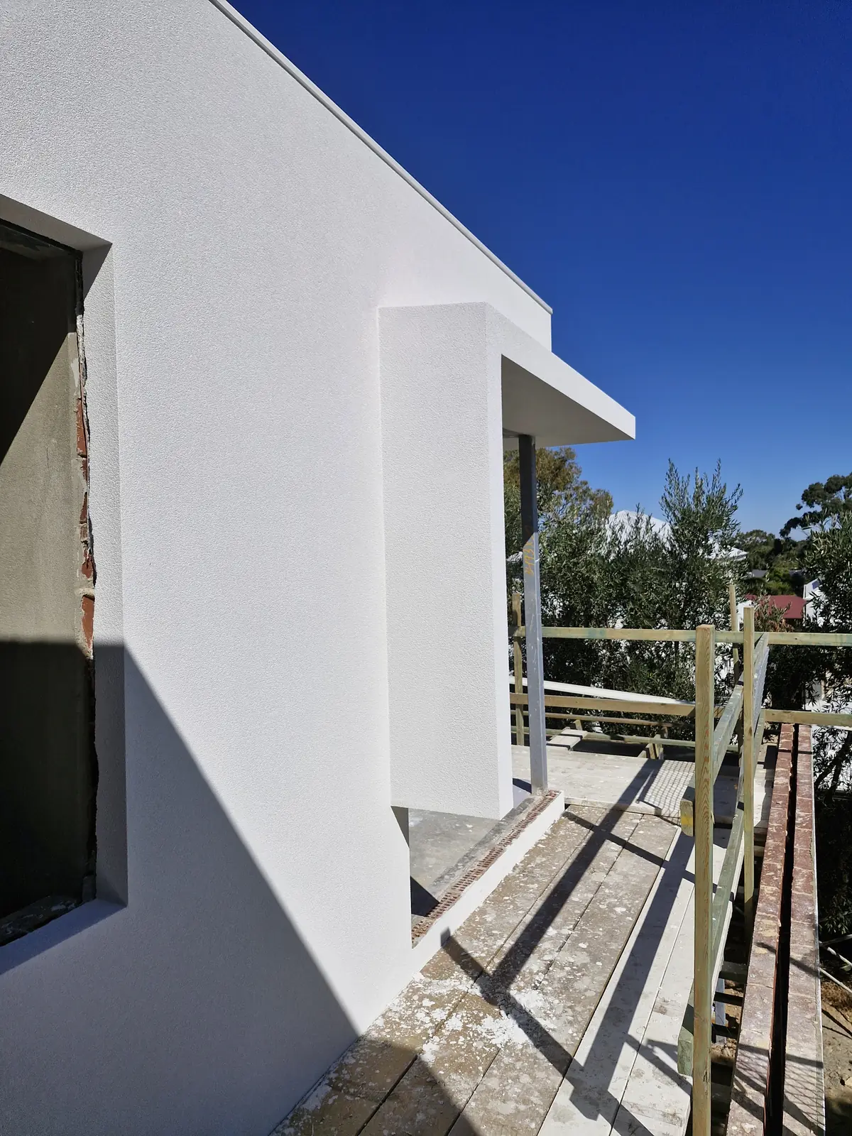 White textured wall and projecting window surround beside a scaffold walkway.