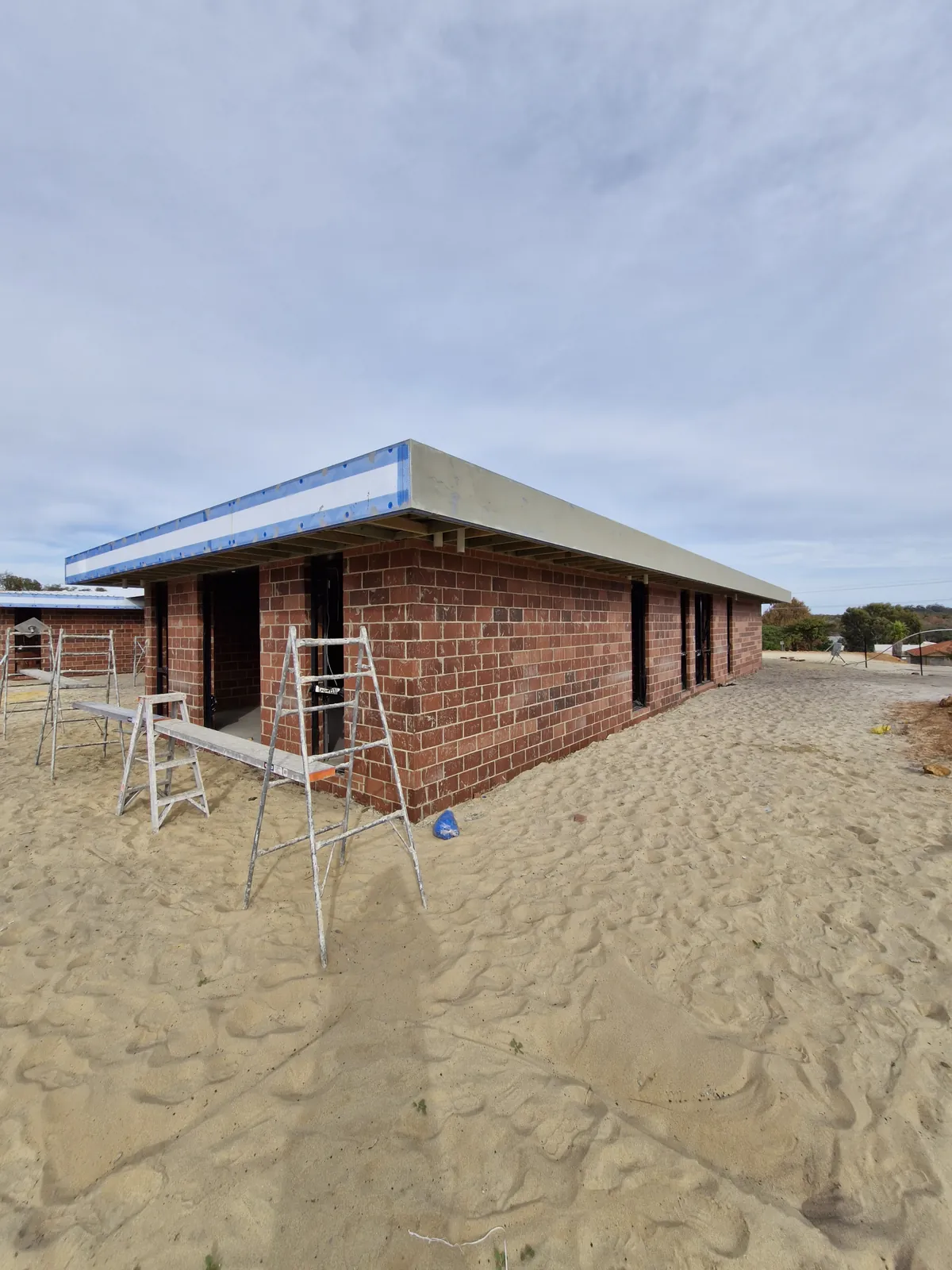 Brick building under construction with pale panels and visible fixing heads around the upper roofline.