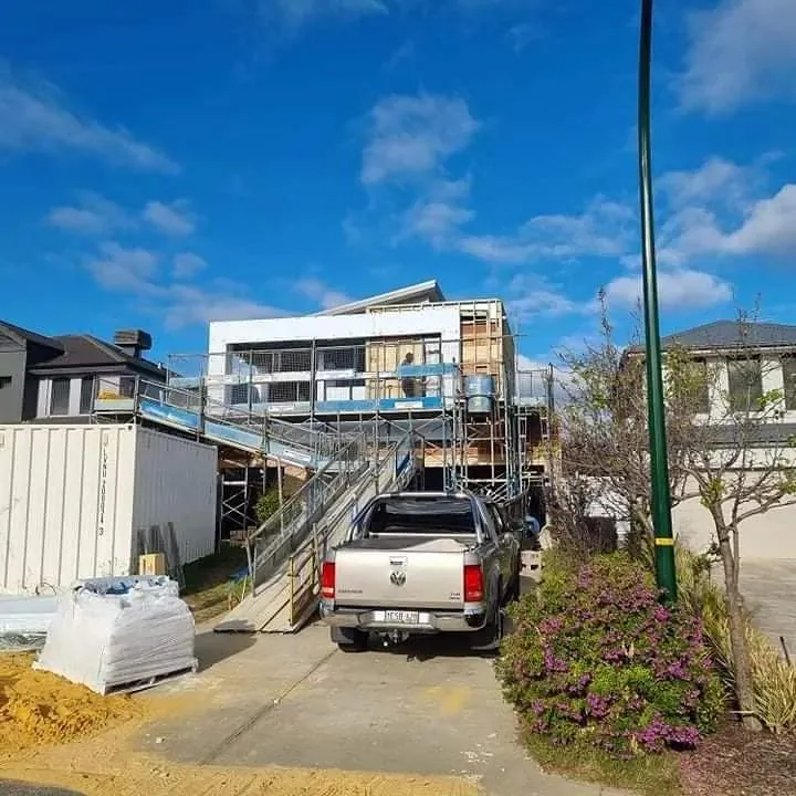 House under construction behind scaffolding, with a ute and building materials in the driveway.