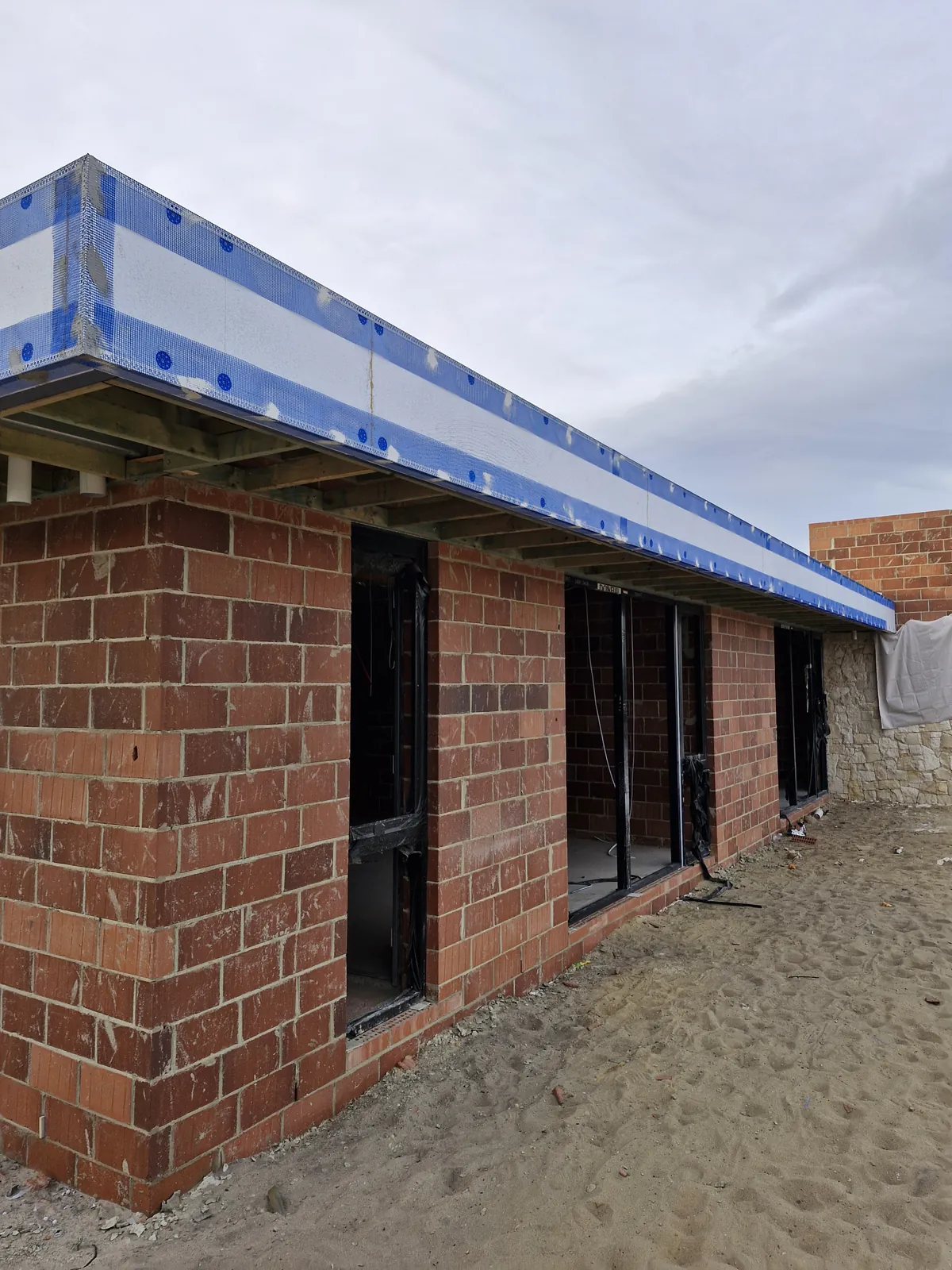 Pale panels and blue fixing heads along a roof edge above unfinished brick walls and door openings.