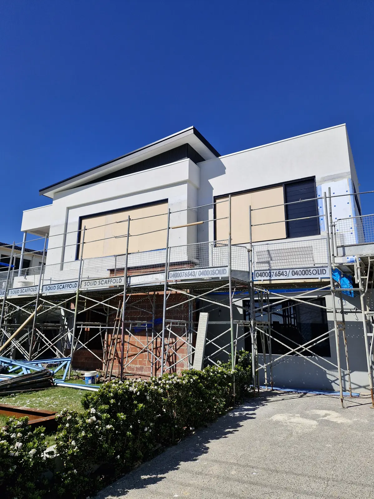 Rendered upper facade and covered window openings above brickwork, with scaffolding still in place.