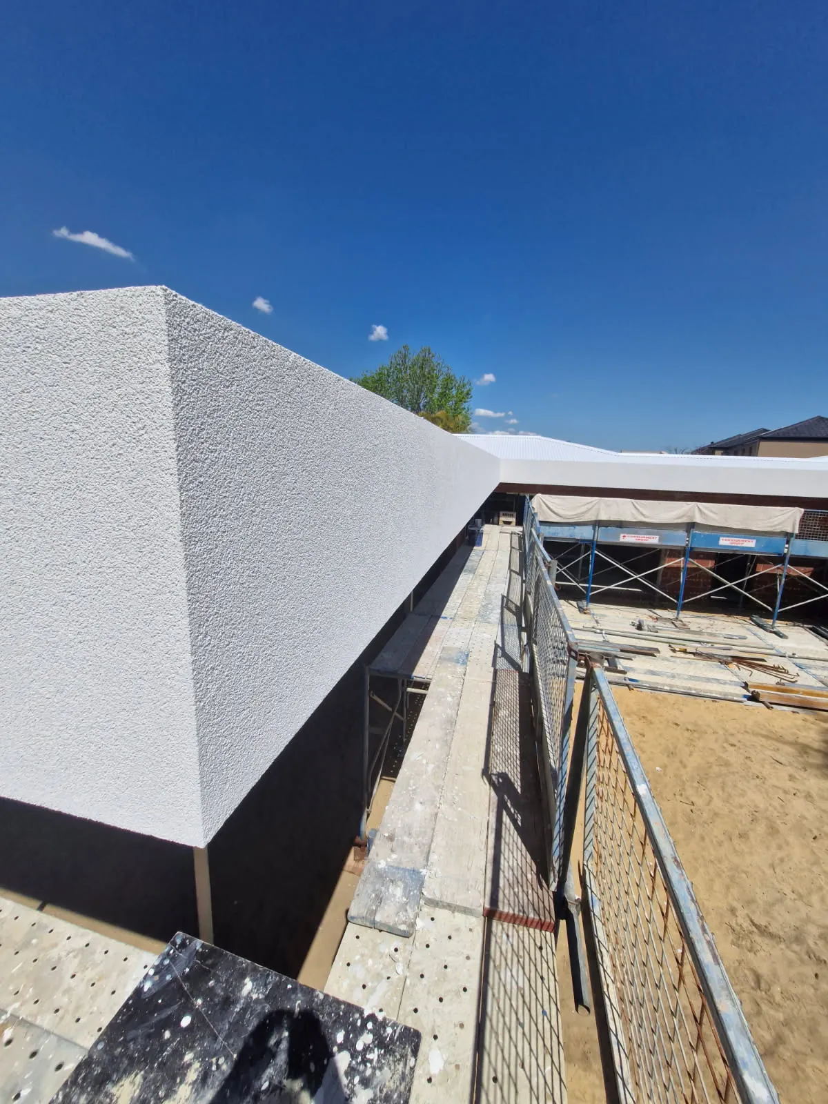 Close view of a white textured parapet edge above a scaffold walkway.