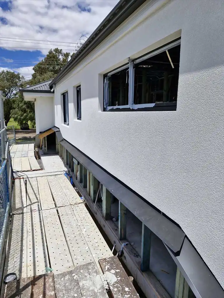 White textured exterior wall around open window frames beside scaffolding.